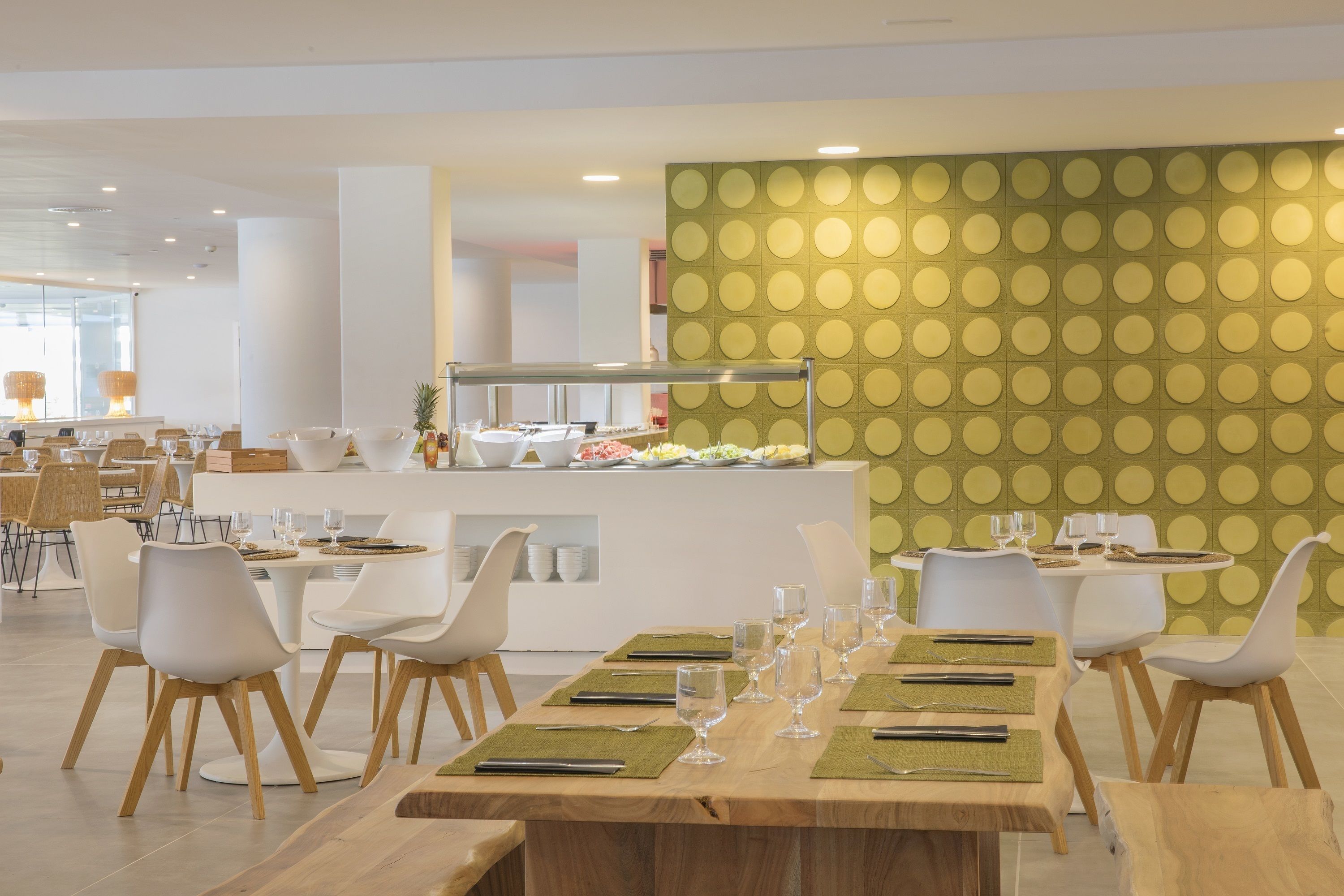 Uma sala de jantar moderna com mesas redondas, cadeiras brancas e um buffet.
