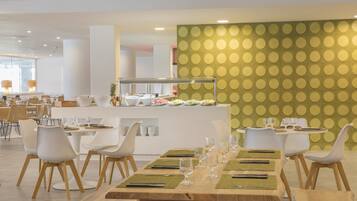Uma sala de jantar moderna com mesas redondas, cadeiras brancas e um buffet.