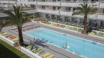 Un espace piscine aménagé sur le toit, avec des chaises longues et des palmiers.