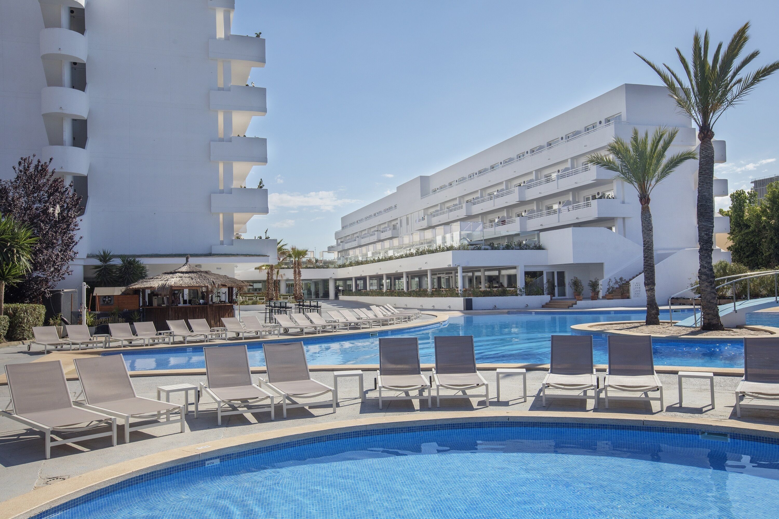 A swimming pool with lounge chairs, a building with multiple balconies, and palm trees.