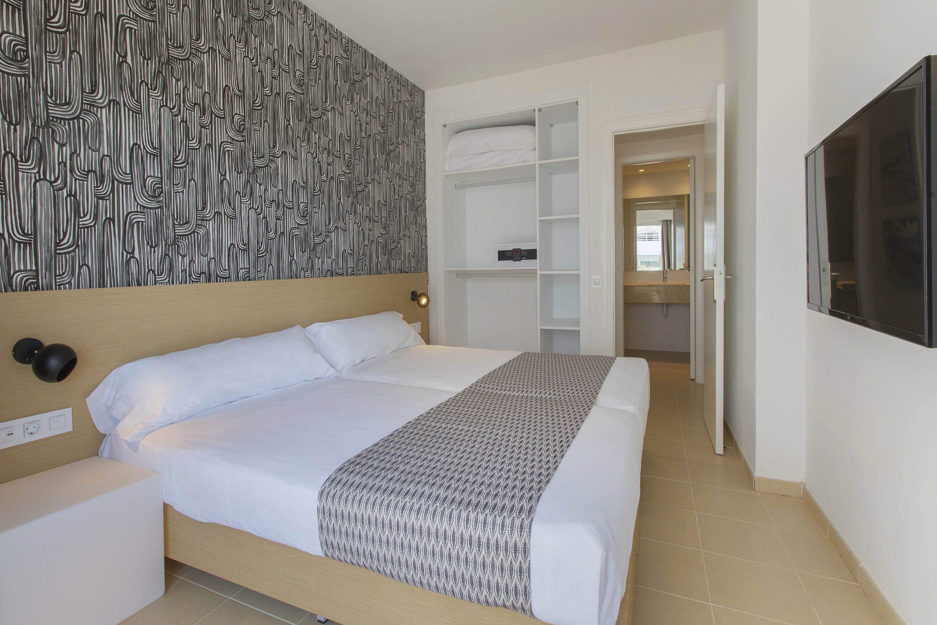A neatly made bed with a patterned blanket, a wall with a black and white abstract design, and a white wardrobe with open doors.