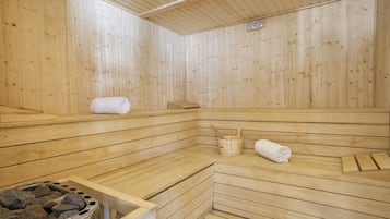 Una sauna de madera con bancos, un balde y un calentador de piedra.