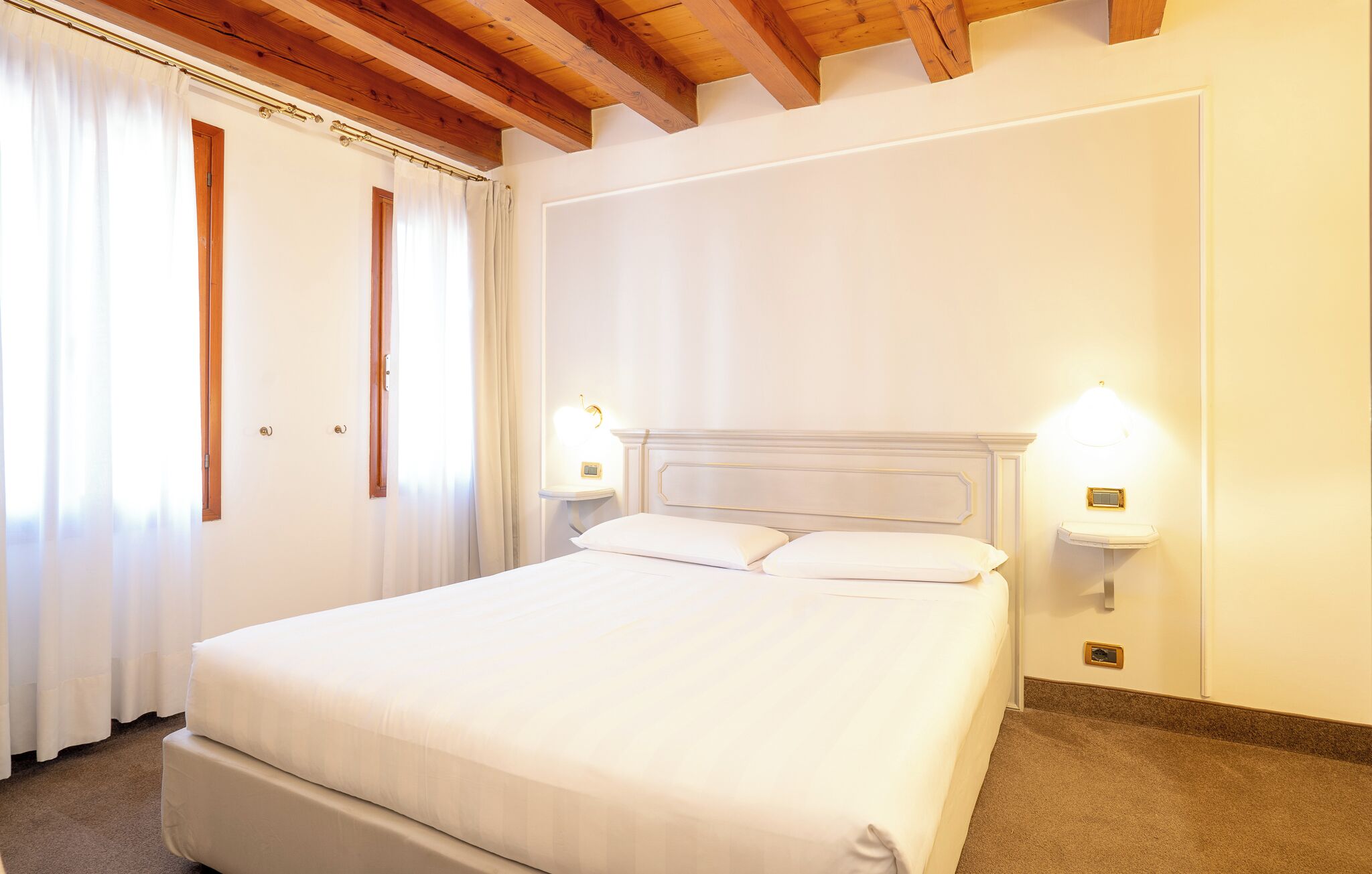 A bedroom with a large bed, white curtains, and two bedside lamps.