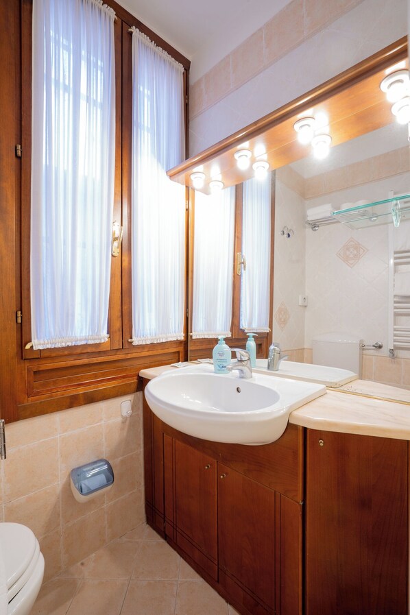A bathroom with wooden cabinets, a white sink, and a mirror with lights above it.