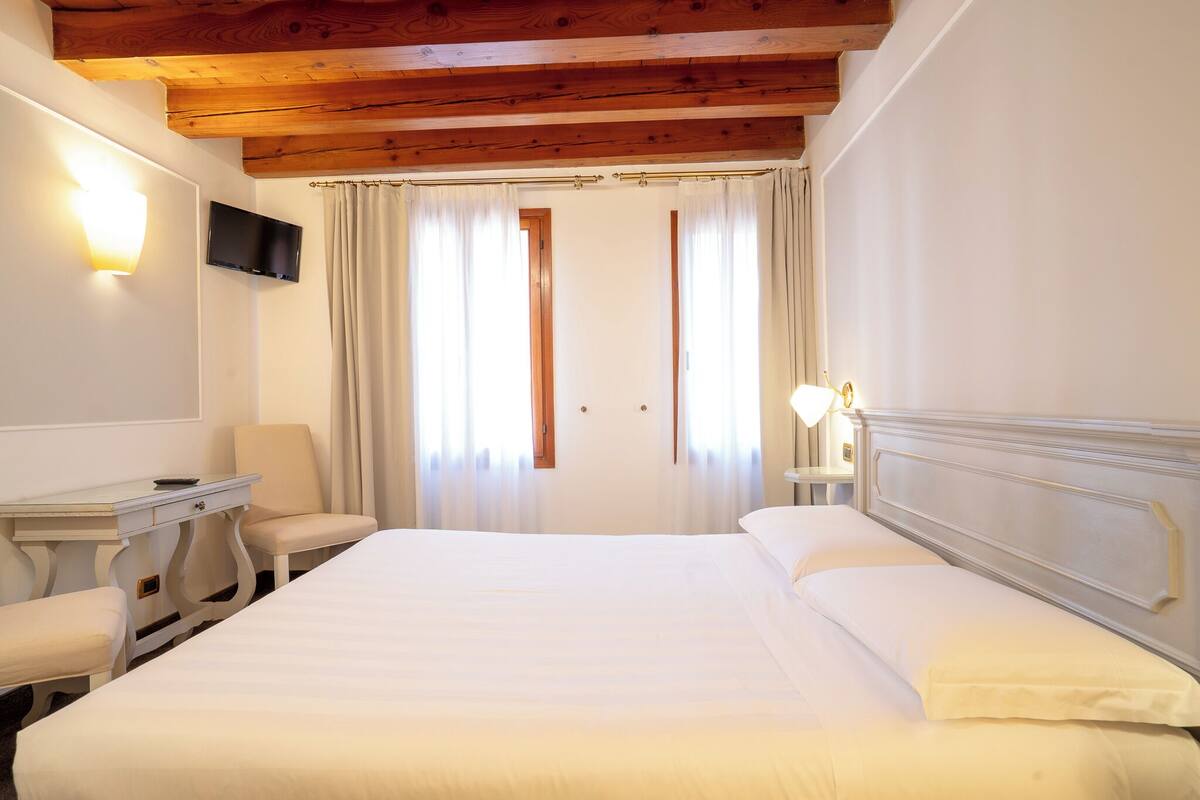 Une chambre d’hôtel avec un lit, un bureau, une chaise, une télévision et une fenêtre avec des rideaux.