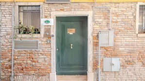 Un edificio de ladrillo con una puerta verde, una ventana con reja de metal y un tapete rojo en el suelo.