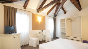 Habitación de hotel con cama, escritorio con silla, televisión, armario y luz empotrada en la pared.