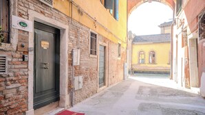 Una calle estrecha con un edificio de ladrillo, destacando una puerta oscura y un felpudo rojo en la entrada.