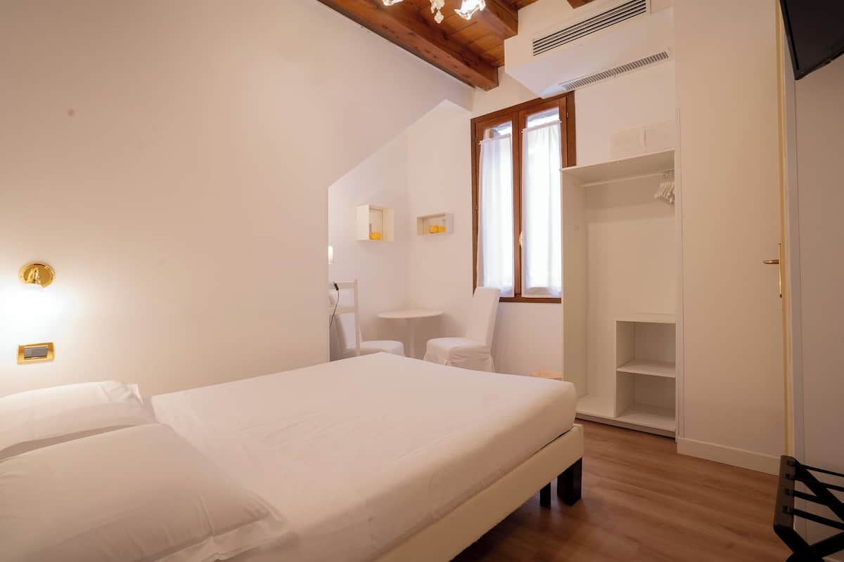 Une chambre à coucher avec un lit, une petite table, une chaise, une armoire et une fenêtre avec des rideaux.
