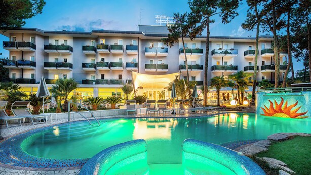 Un hotel con piscina, mobiliario exterior y un edificio con varios balcones.
