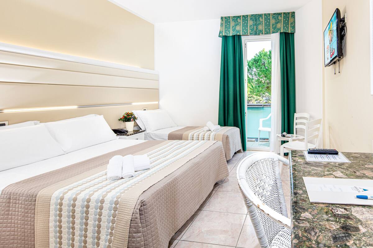 Habitación de hotel con dos camas, un escritorio con silla, televisión y vistas al exterior.