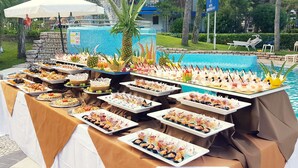 Una mesa de buffet con diferentes platillos y una piscina al fondo.