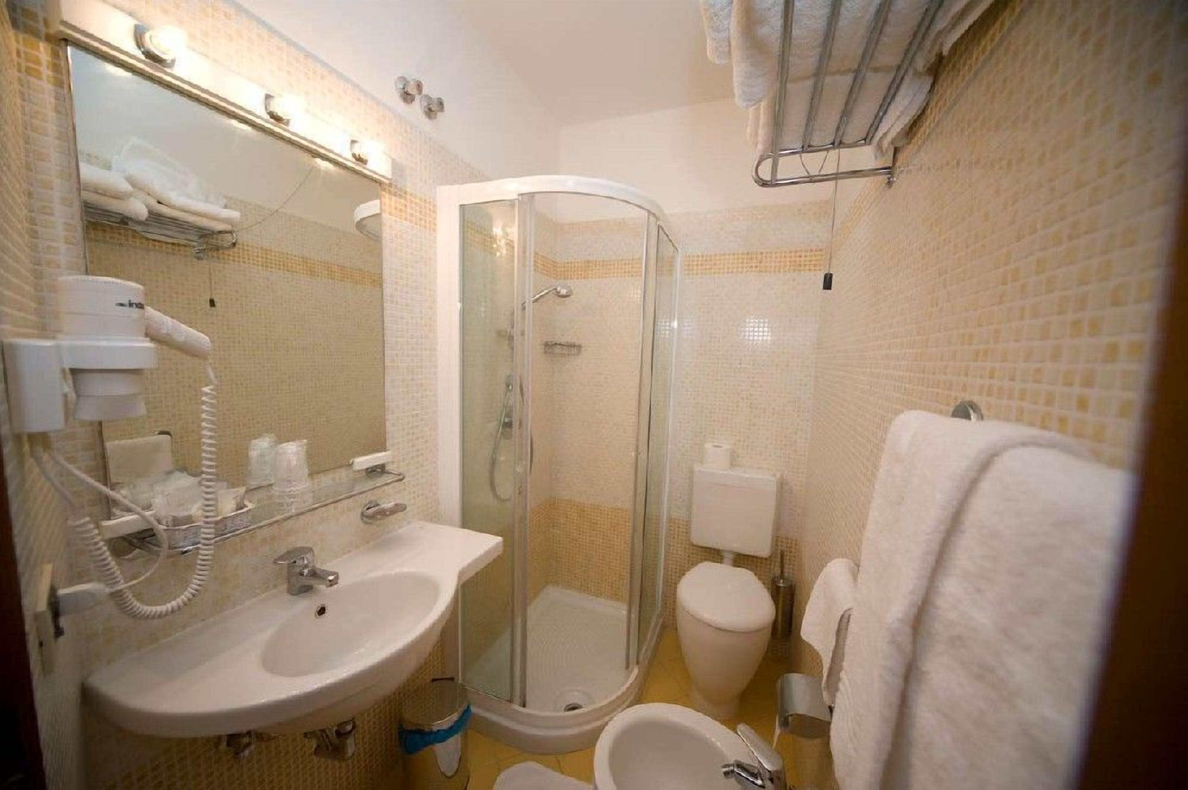 A bathroom with a glass-enclosed shower, a sink, a toilet, and a mirror with lights.