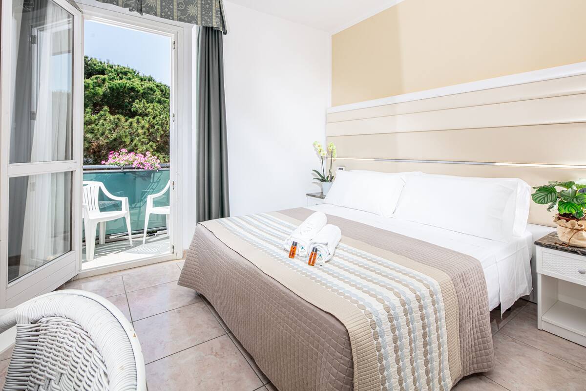 Habitación de hotel con cama, mesita de noche, una silla y vistas al exterior.