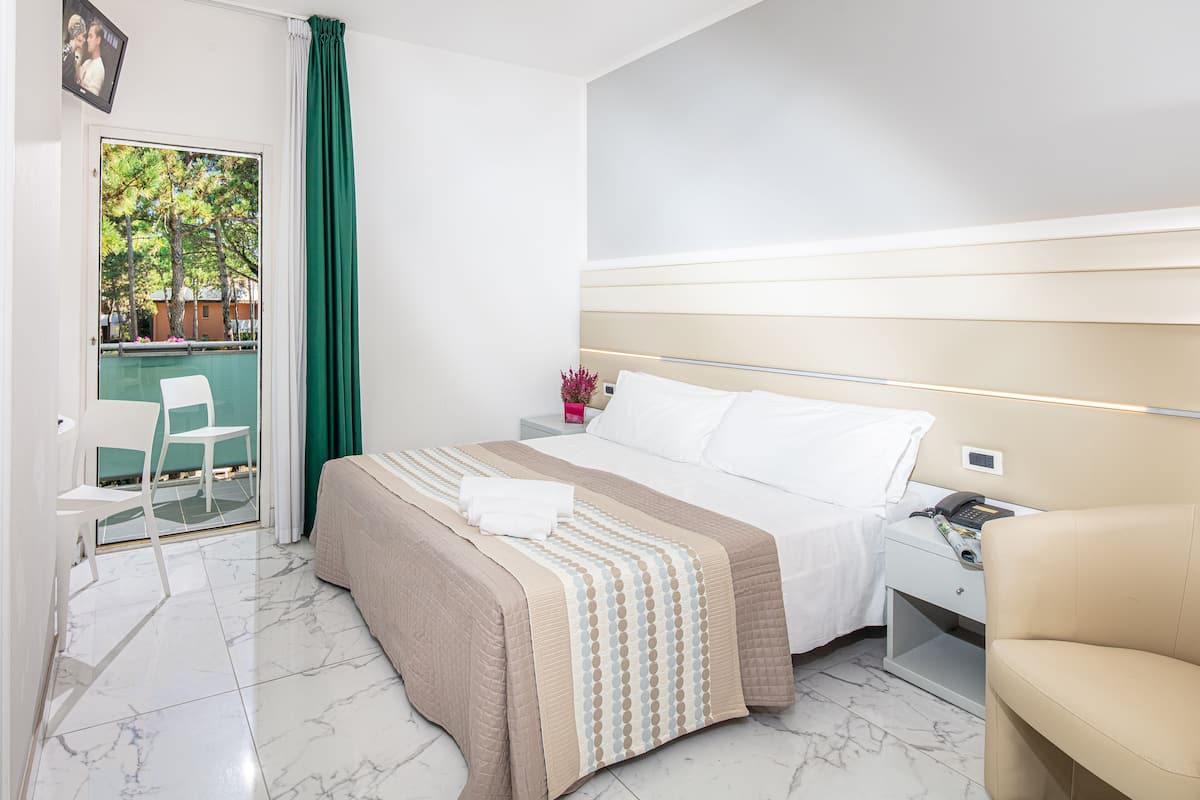 Habitación de hotel con cama, mesita de noche con teléfono, una silla y vista a una piscina a través de una puerta de vidrio.