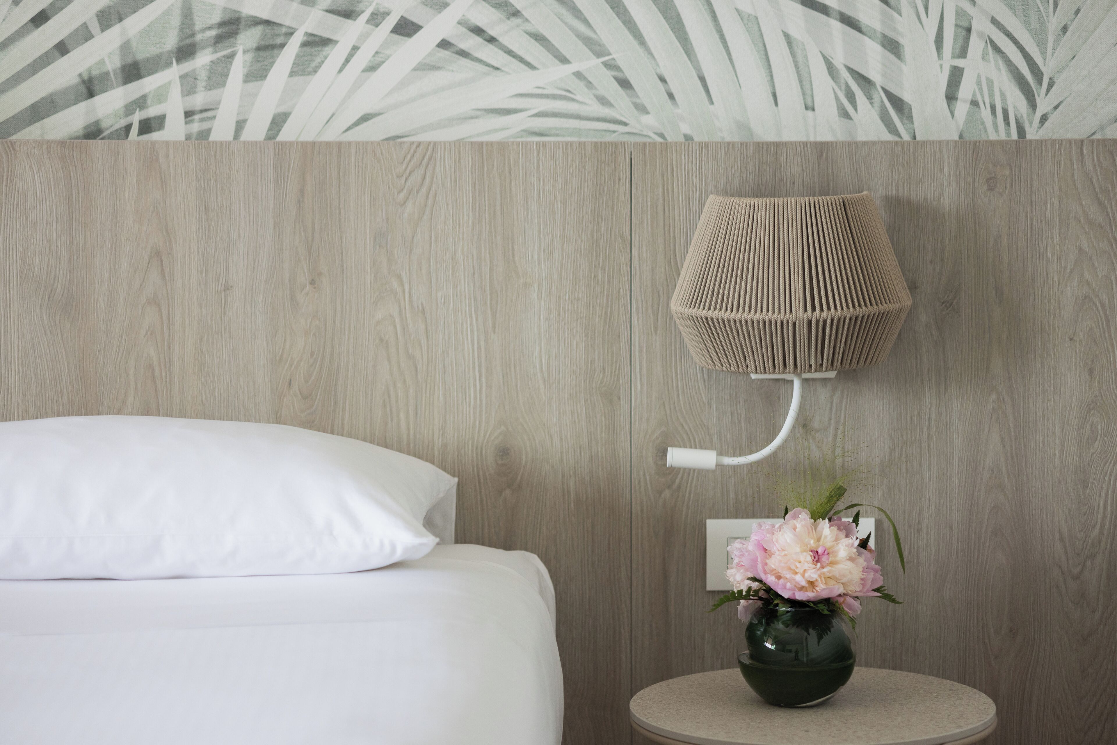 Un dormitorio con una cama, una lámpara de pared y un florero con flores.