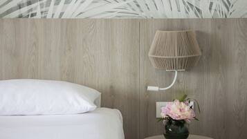 Un dormitorio con una cama, una lámpara de pared y un florero con flores.