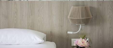 A bedroom with a bed, a wall-mounted lamp, and a vase with flowers.
