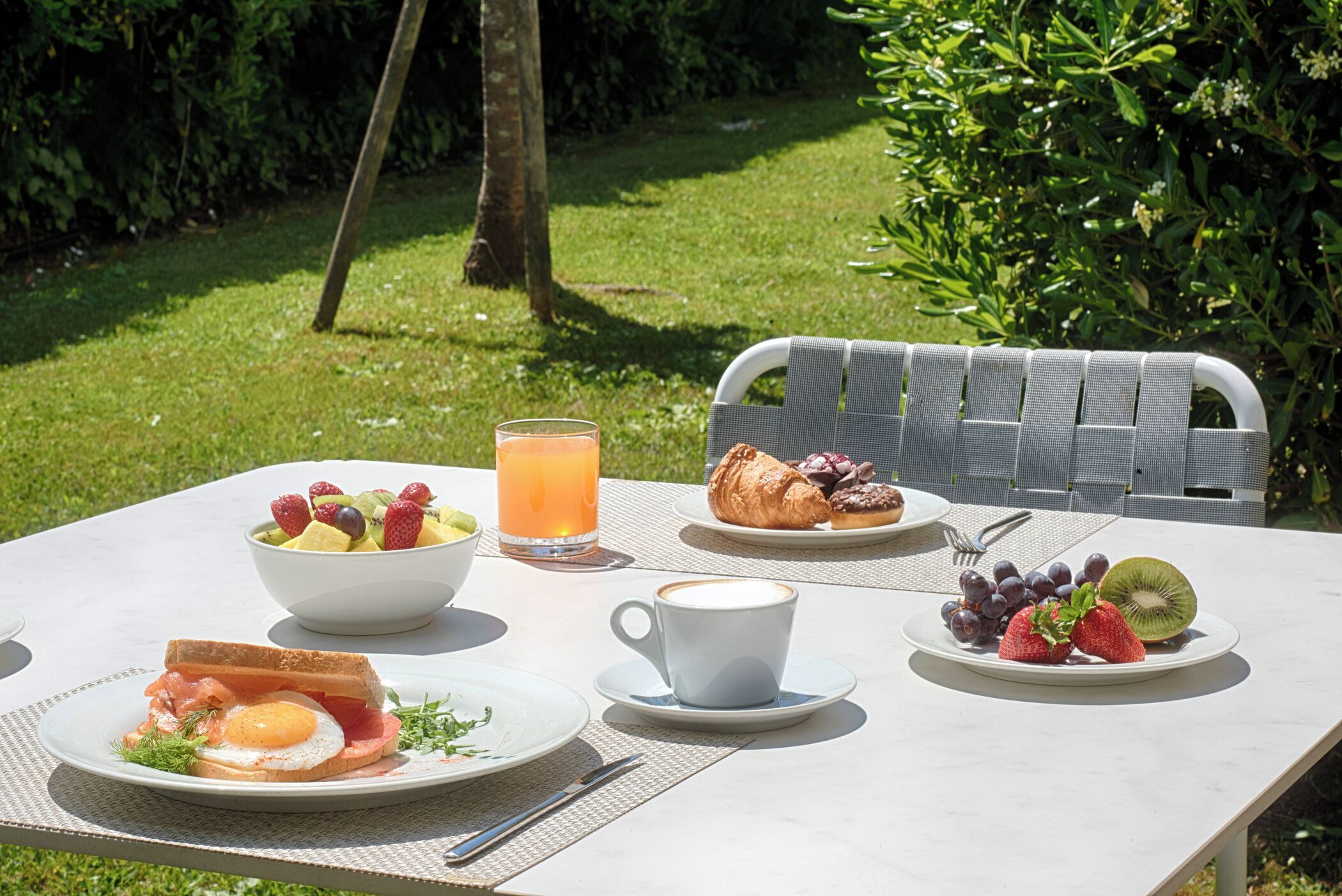 Una mesa dispuesta para el desayuno con tostadas, huevos, fruta y un croissant, junto a un vaso de jugo de naranja.