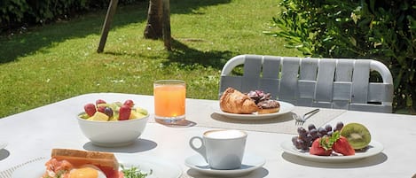 Una mesa dispuesta para el desayuno con tostadas, huevos, fruta y un croissant, junto a un vaso de jugo de naranja.