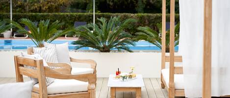 Una terraza de madera con piscina, sillones de descanso y sombrillas.