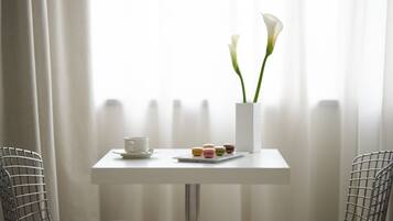 A small table with a white vase containing two white flowers, a cup, and a tray of colorful macarons.