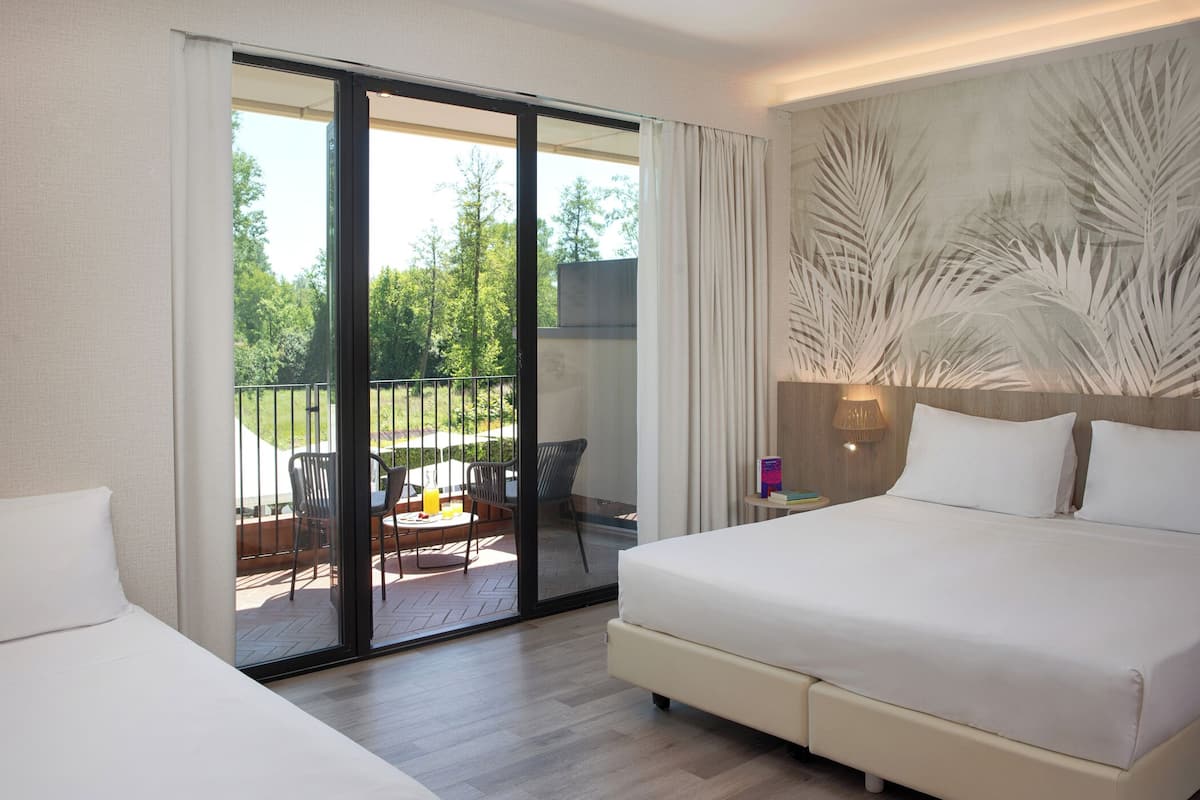 A hotel room with a large bed, a sliding glass door to an outdoor patio, and a wall with a palm leaf design.