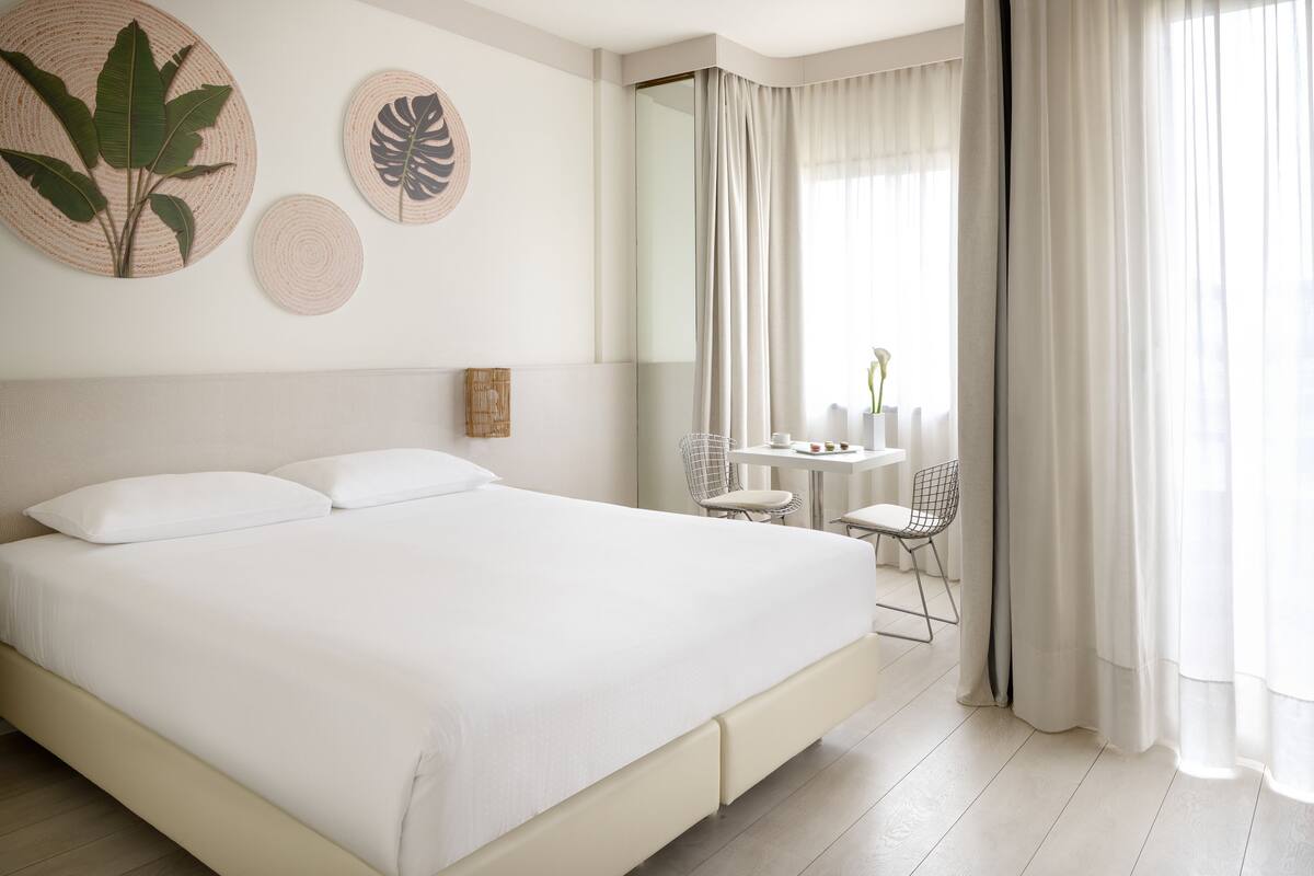 A large bed with white linens, a small table with chairs, and two wall-mounted decorative items.