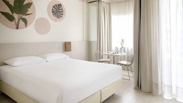 A large bed with white linens, a small table with chairs, and two wall-mounted decorative items.