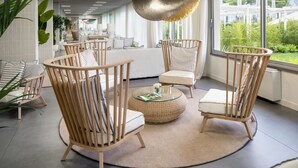 Sala de estar moderna com mesa de centro redonda de vidro, poltronas estofadas listradas e vista para o verde lá fora.