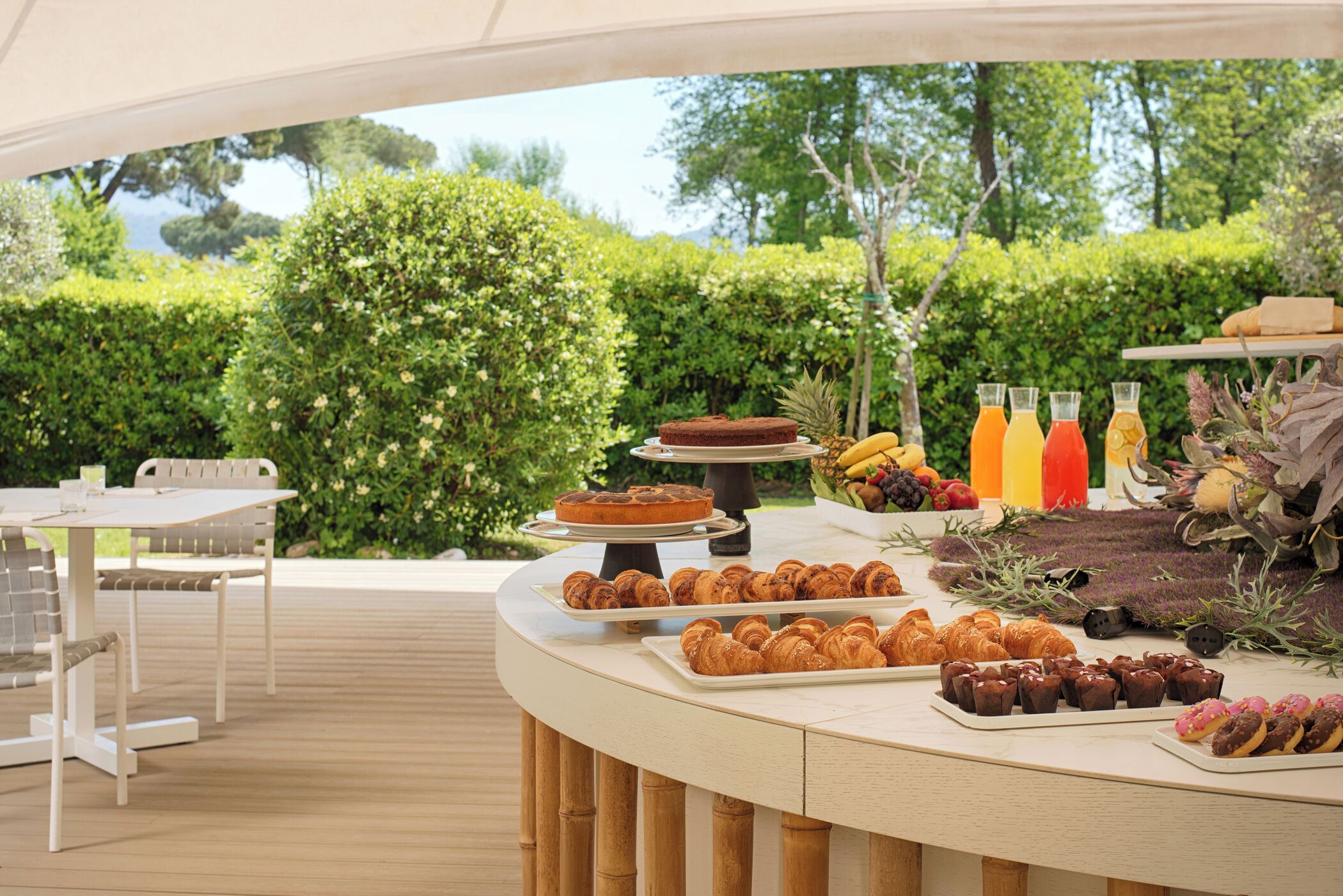 Un bufé al aire libre con diversos pasteles, frutas y bebidas sobre una terraza de madera.