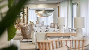 Uma sala de estar moderna com um sofá, cadeiras de madeira, uma mesa de jantar e um lustre.