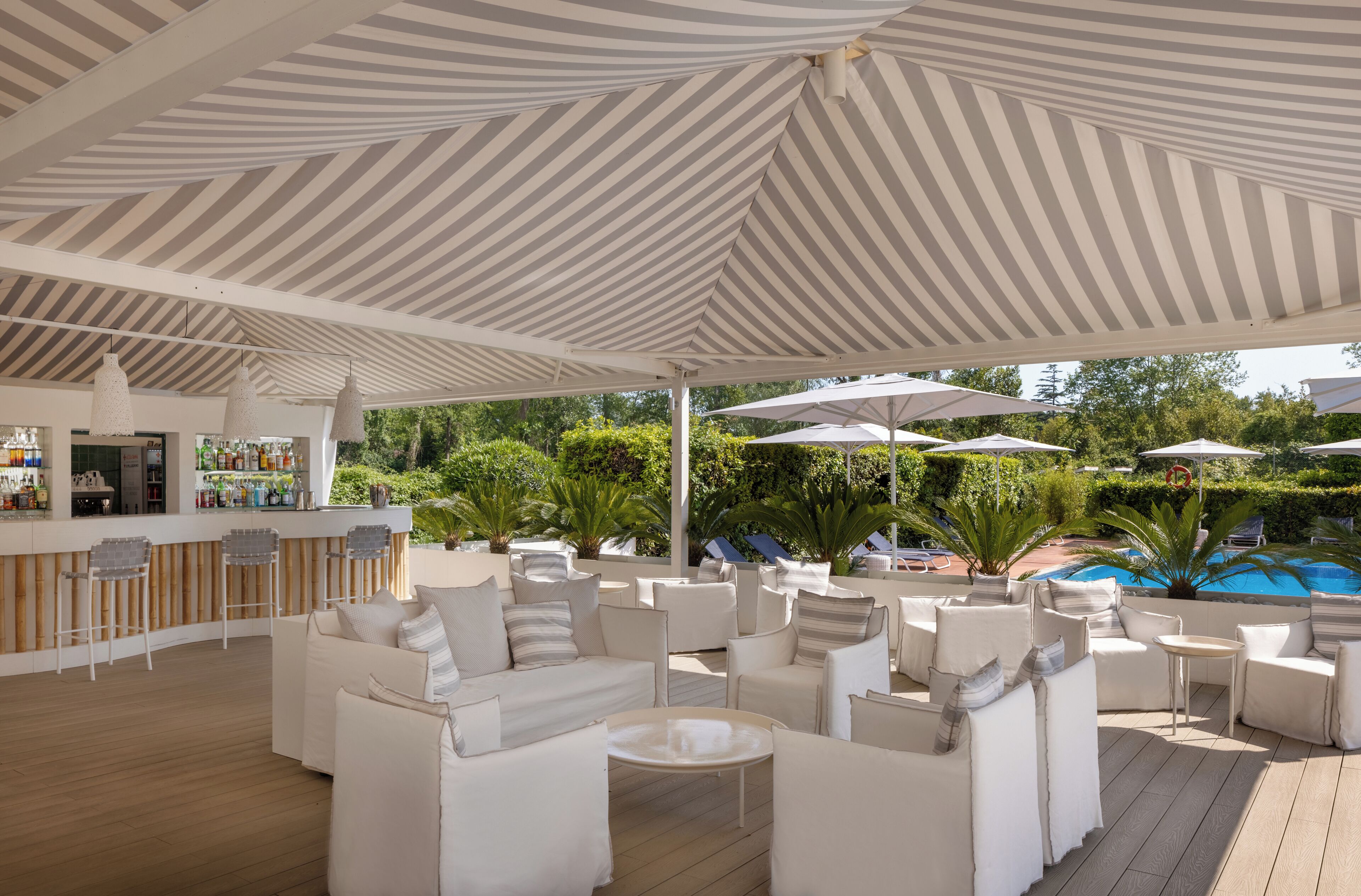 A covered outdoor seating area with white furniture and a bar.