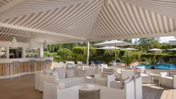 A covered outdoor seating area with white furniture and a bar.