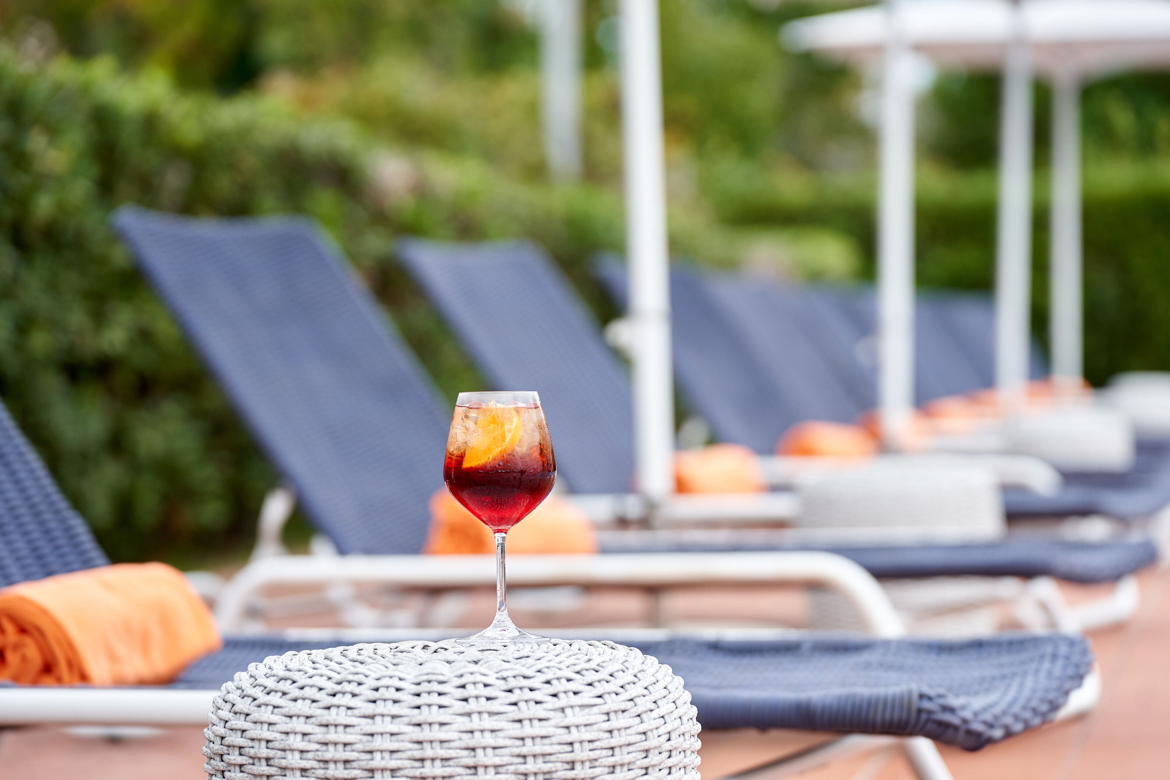 A lounge area with a wicker chair, a glass of drink, and a poolside setting.