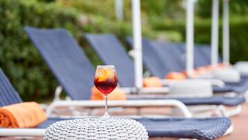 Un espace détente avec un fauteuil en osier, un verre et une vue sur la piscine.