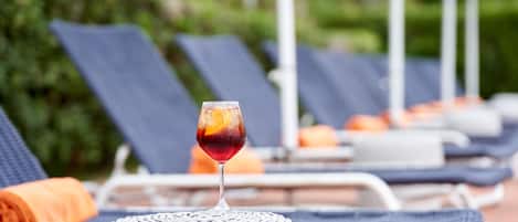 A lounge area with a wicker chair, a glass of drink, and a poolside setting.