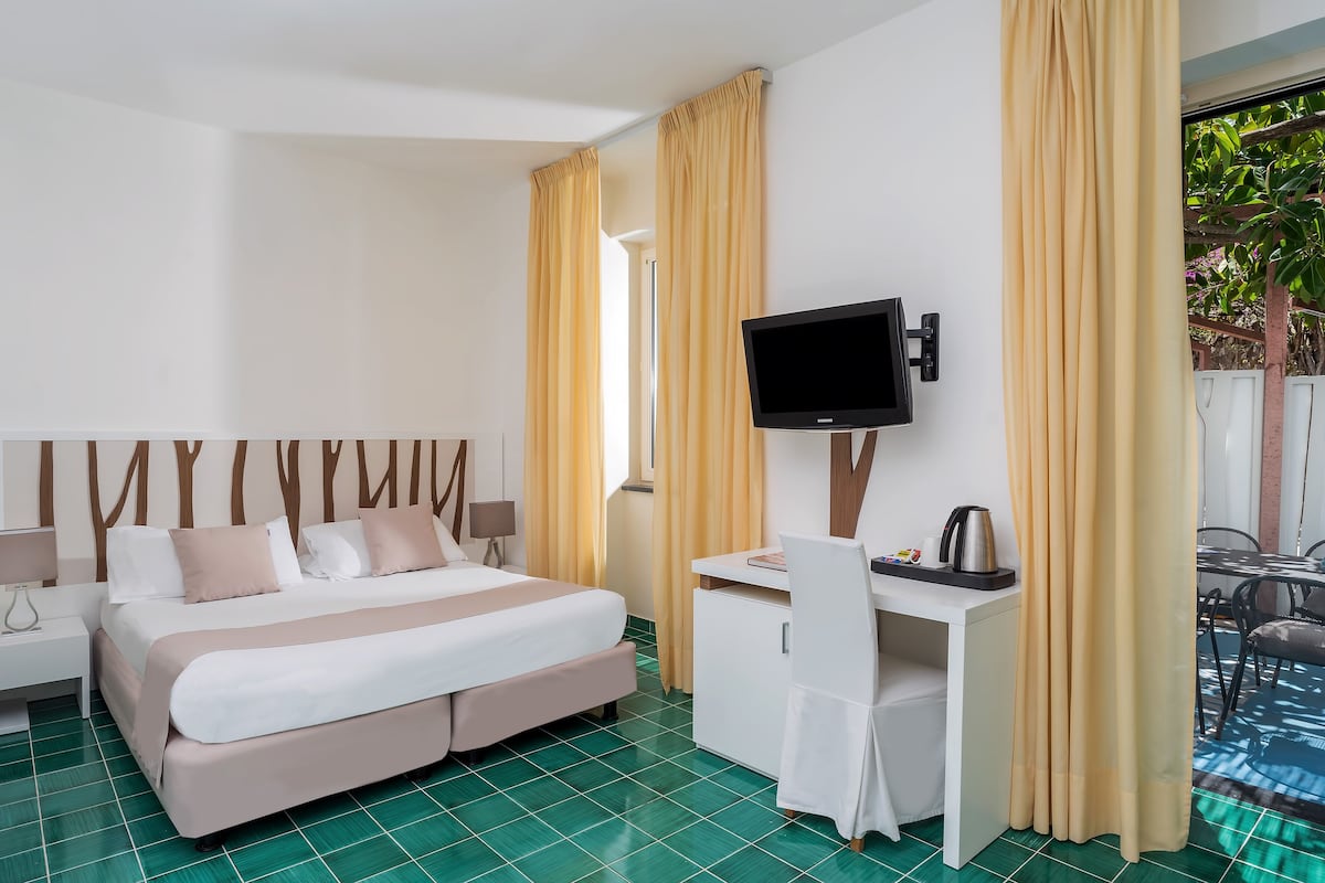 A hotel room with a bed, desk, TV, and curtains.