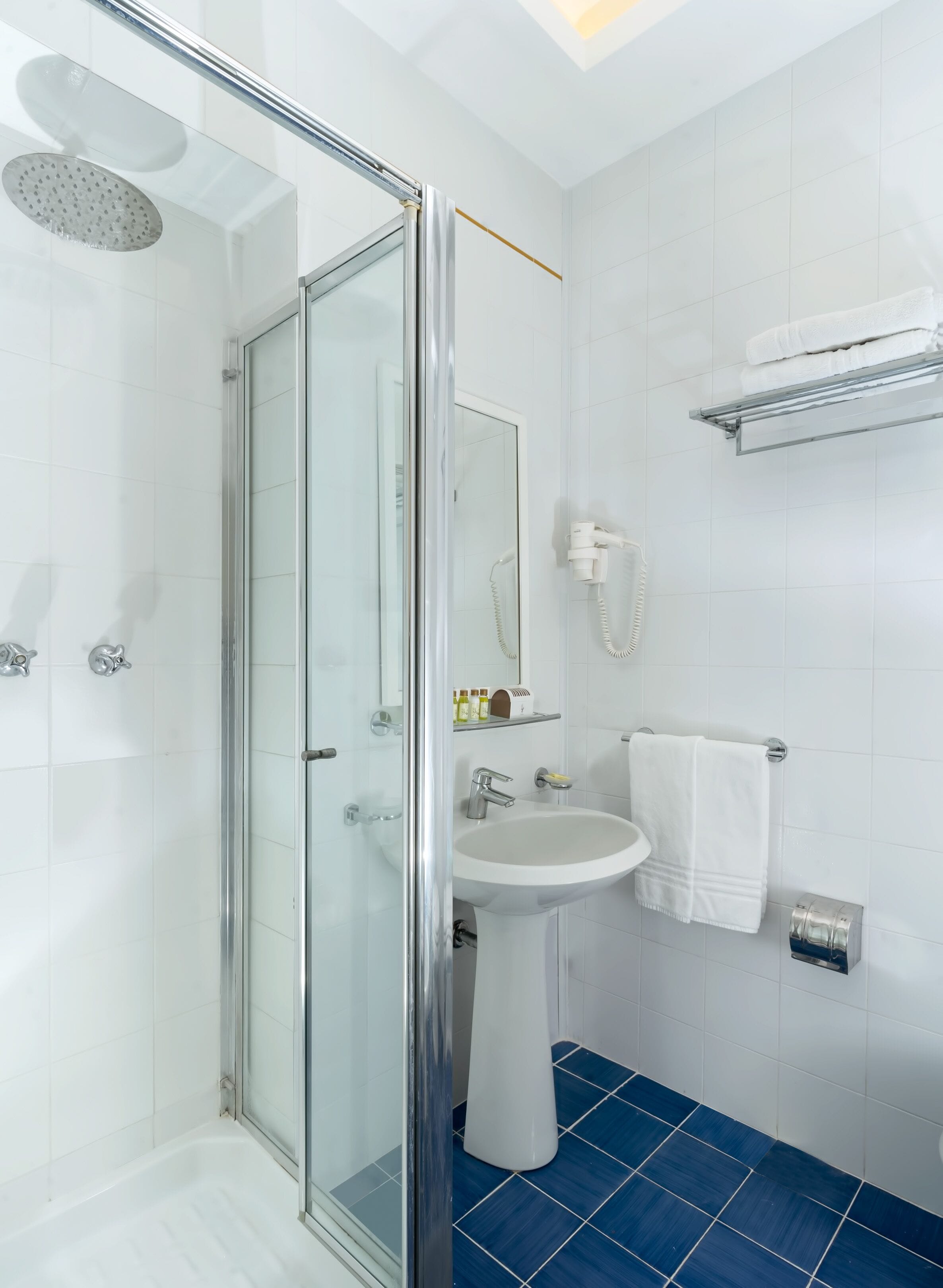 A modern bathroom with a glass-enclosed shower, a white sink, and a blue-tiled floor.