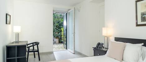 Ein Hotelzimmer mit Bett, Schreibtisch, Stuhl und Blick auf einen Garten durch eine offene Tür.