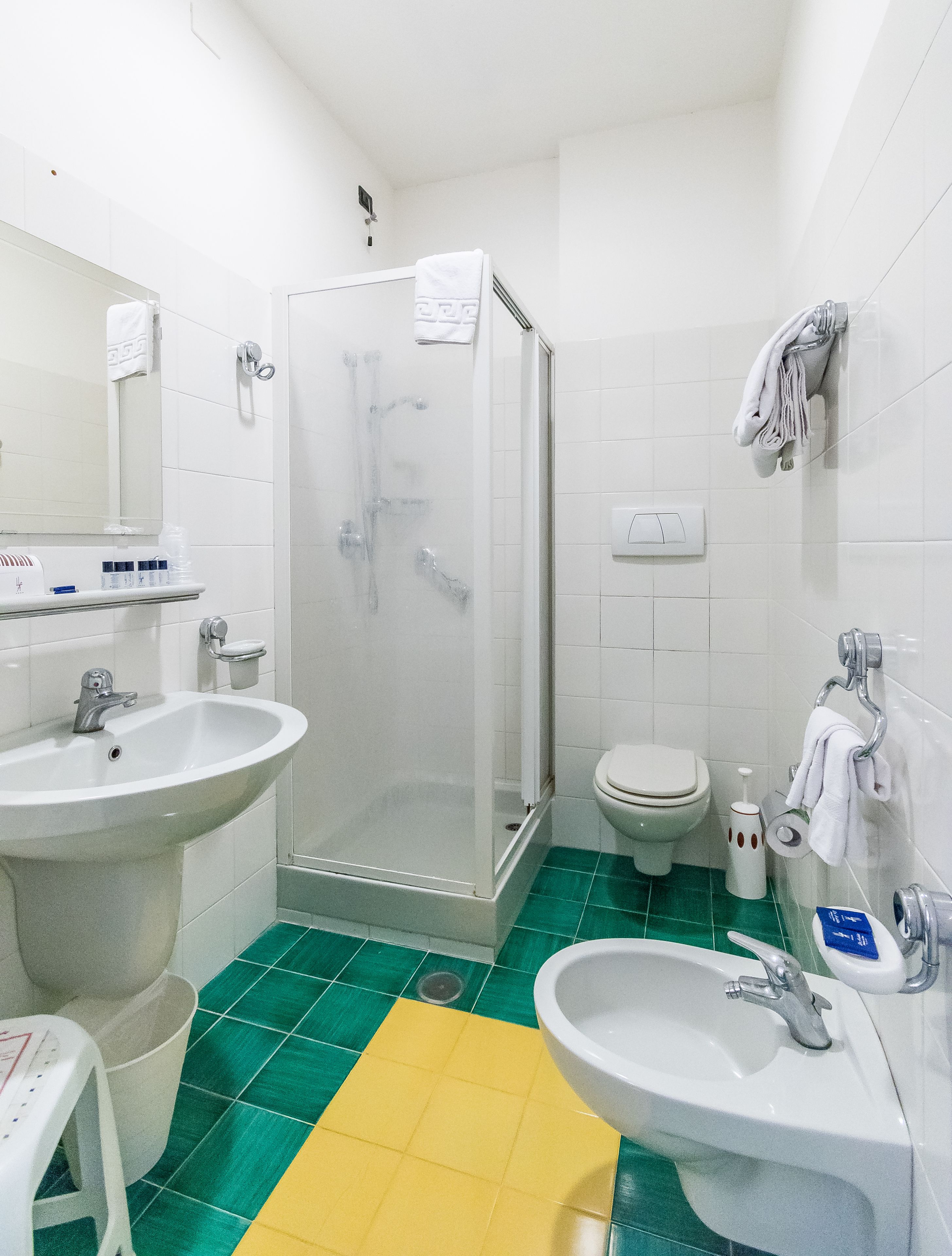 Et badeværelse med brusebad, vask, toilet og en gul gulv måtte.