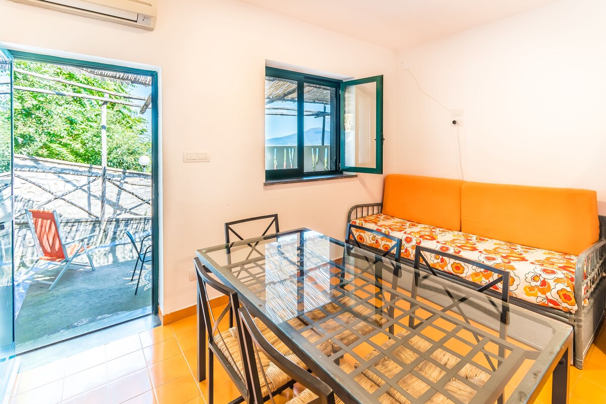 A compact room with a glass table, a sofa, and a window overlooking a balcony.