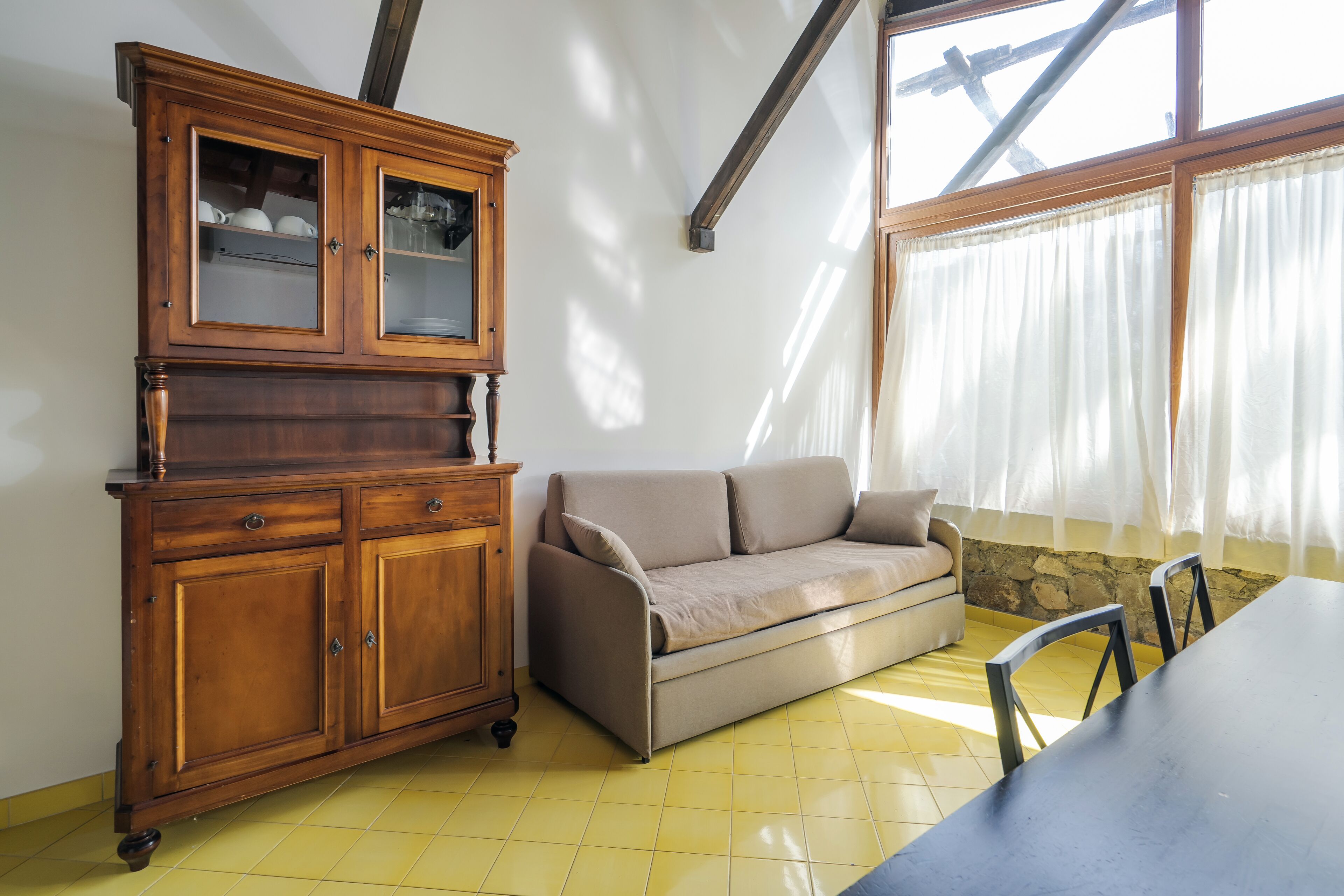 Une pièce comprenant un meuble en bois, un canapé beige, une table à manger et une fenêtre avec des rideaux.