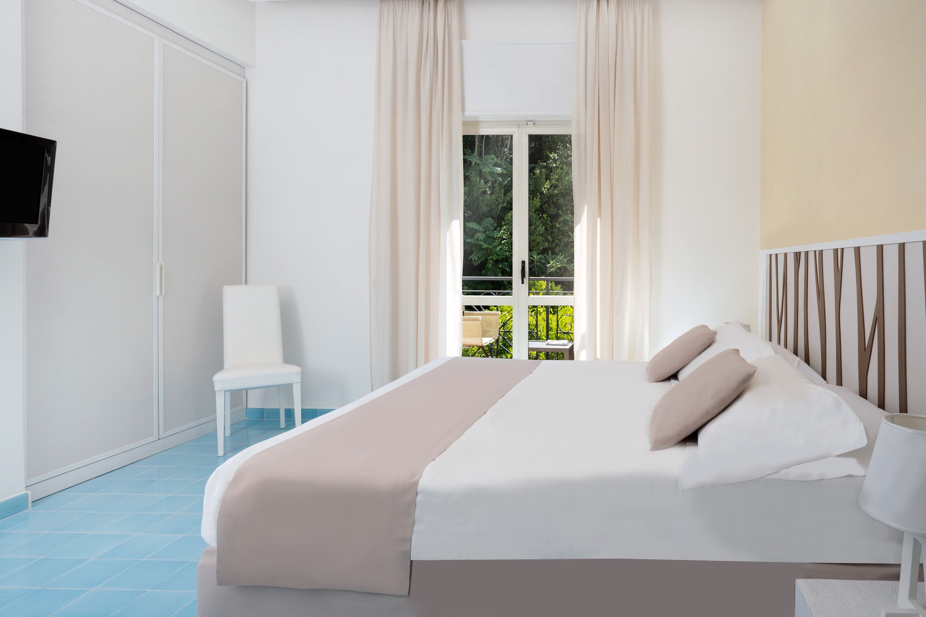 Une chambre à coucher avec un lit, une chaise, une télévision et une fenêtre avec des rideaux.