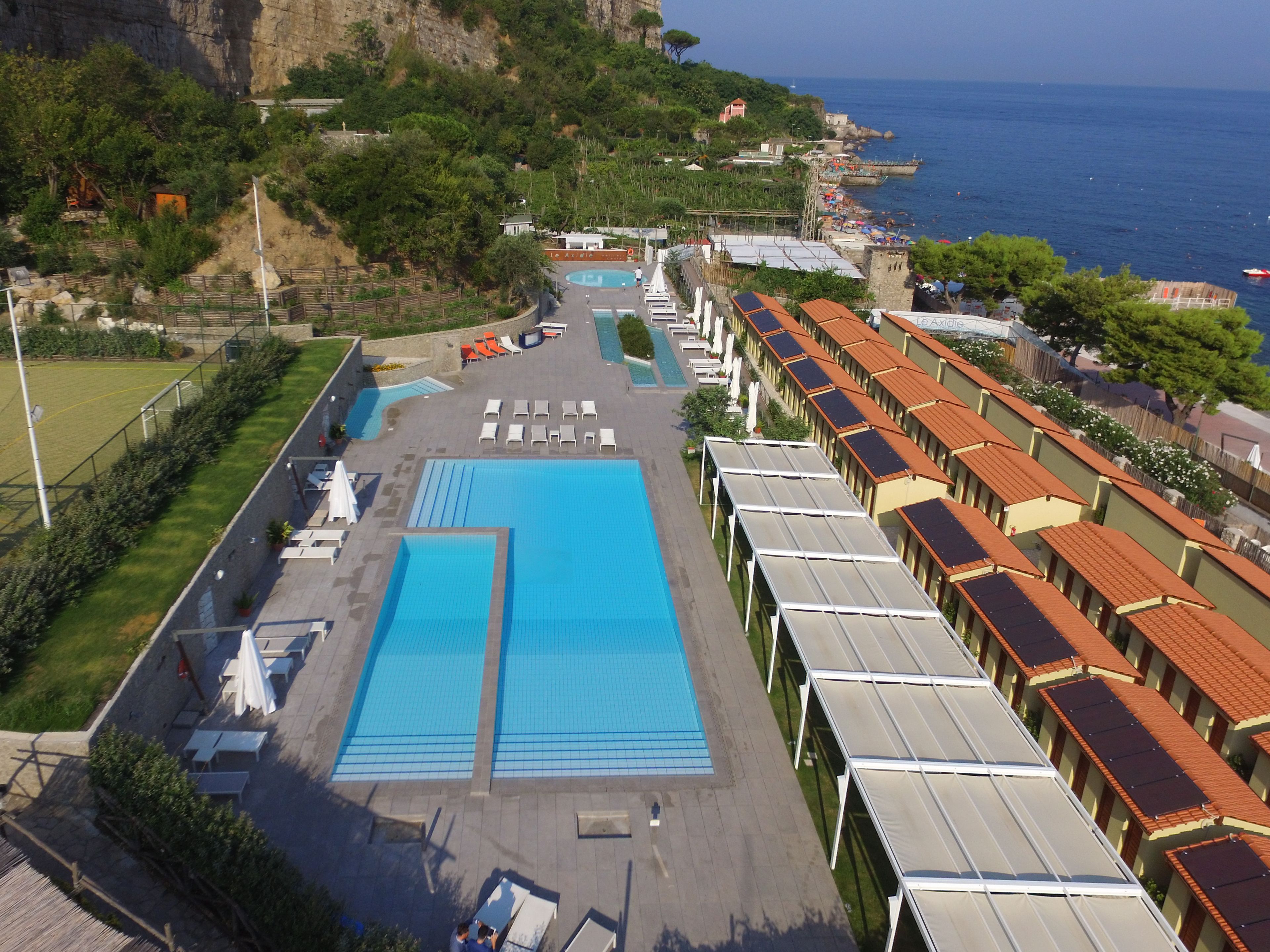 A resort with a large swimming pool, sun loungers, and a view of the sea.