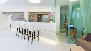 A modern reception area with a white counter, several chairs, and a glass partition. - Hotel & Resort Le Axidie (Vico Equense)