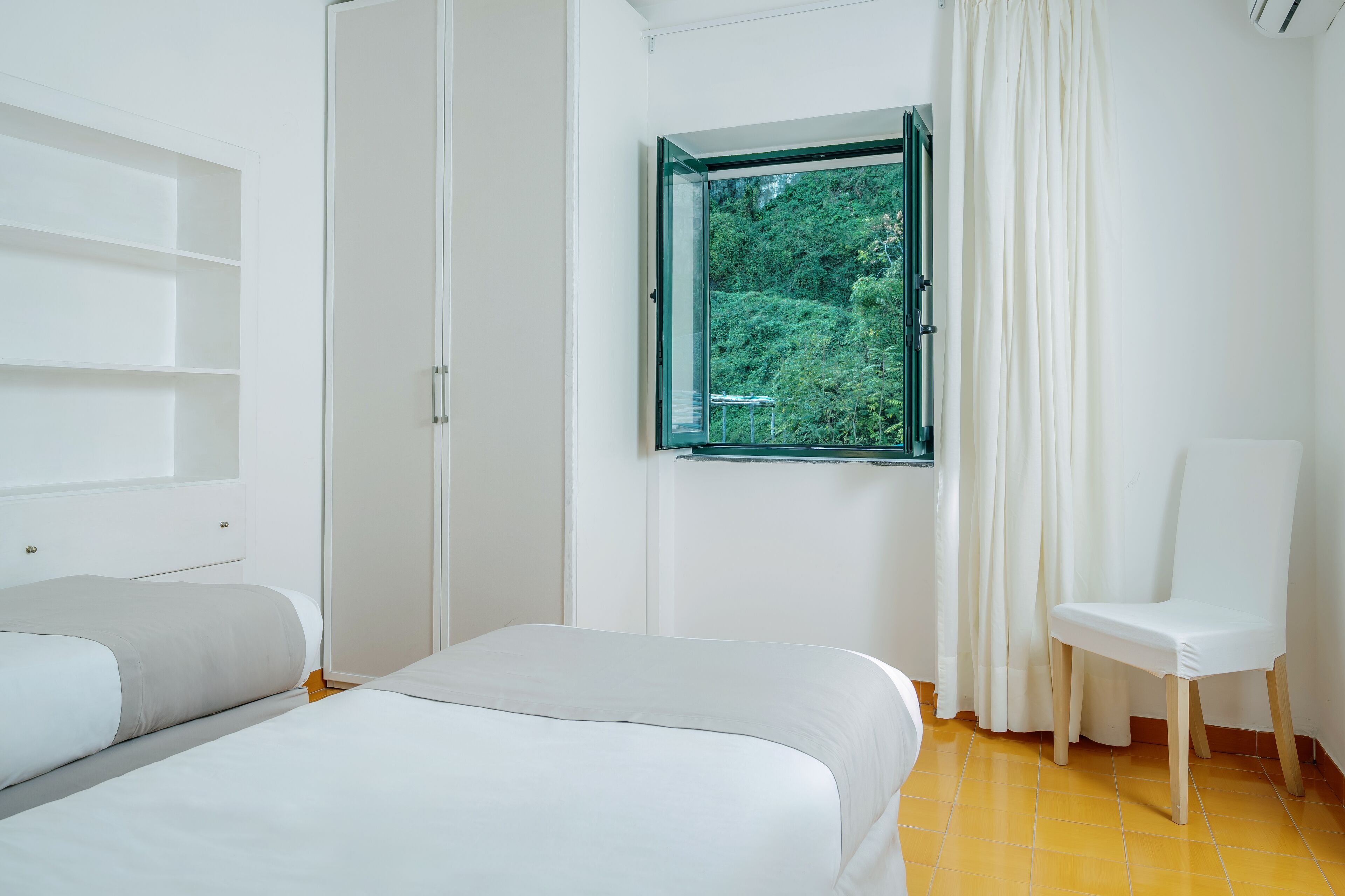 Une chambre à coucher comprenant un lit, une chaise, une armoire et une fenêtre donnant sur un paysage verdoyant.