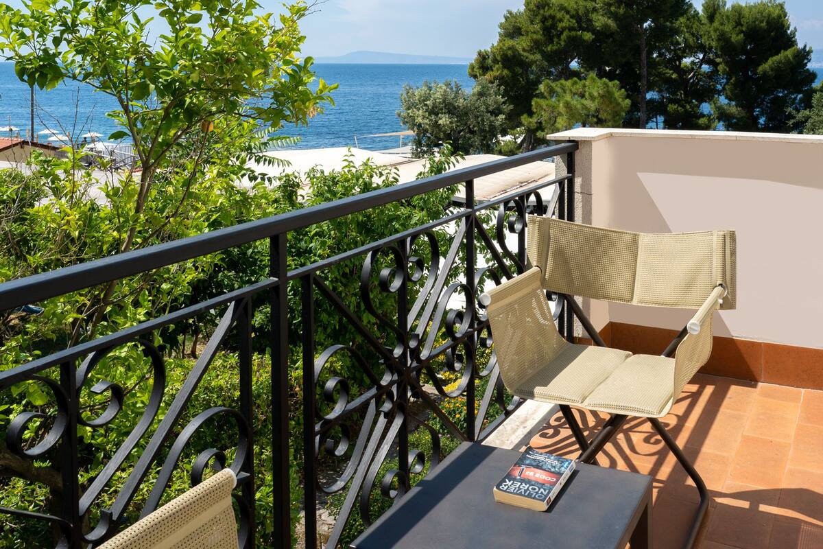 A balcony with wicker furniture, a table, and a view of the sea.
