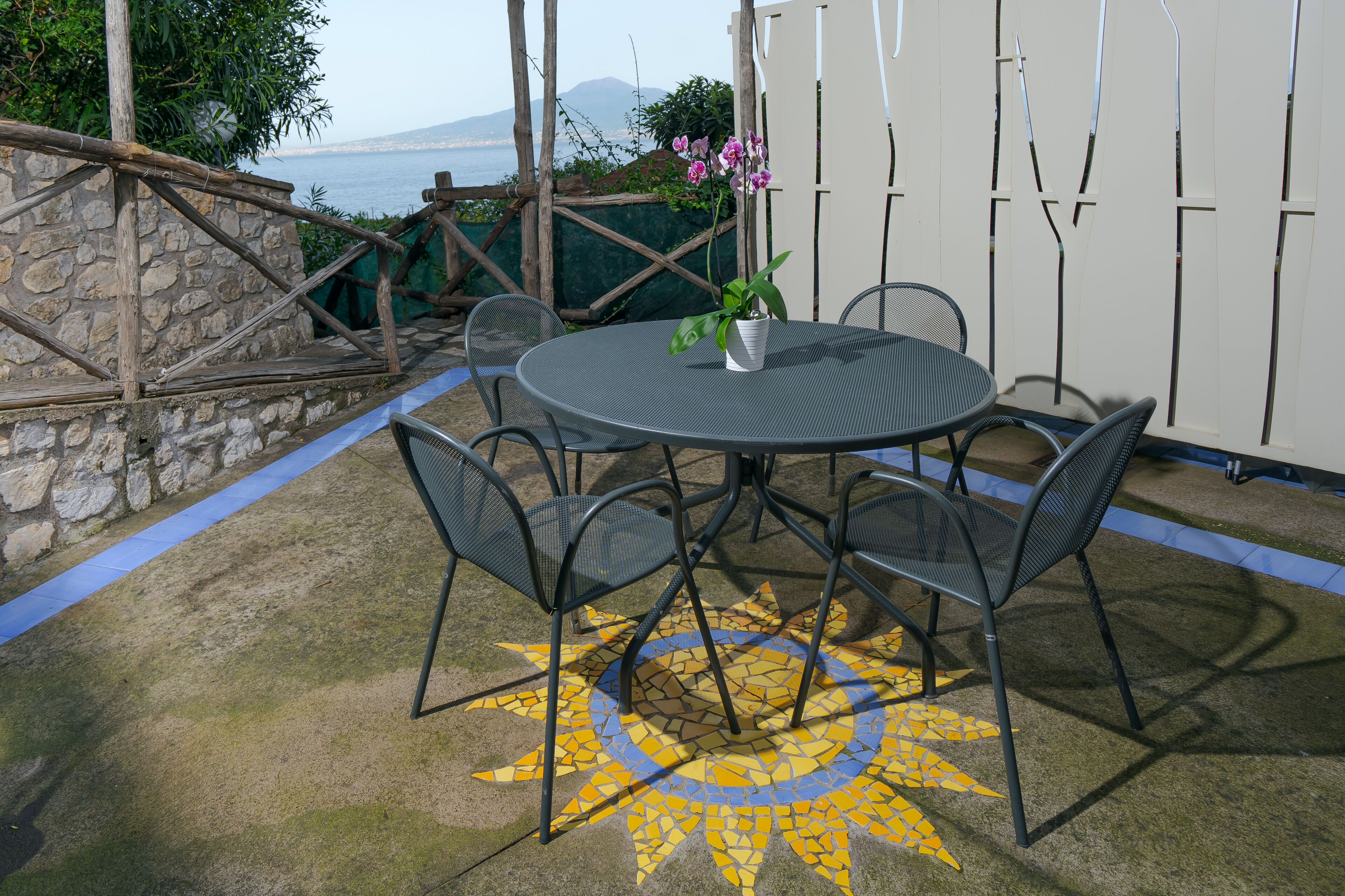 Een ronde metalen tafel met vier stoelen, een orchidee in een pot en een vloer met een zonmotief.