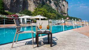 A poolside area with lounge chairs and a table, a clear view of the sea, and a rocky cliff in the background. - Hotel & Resort Le Axidie (Vico Equense)